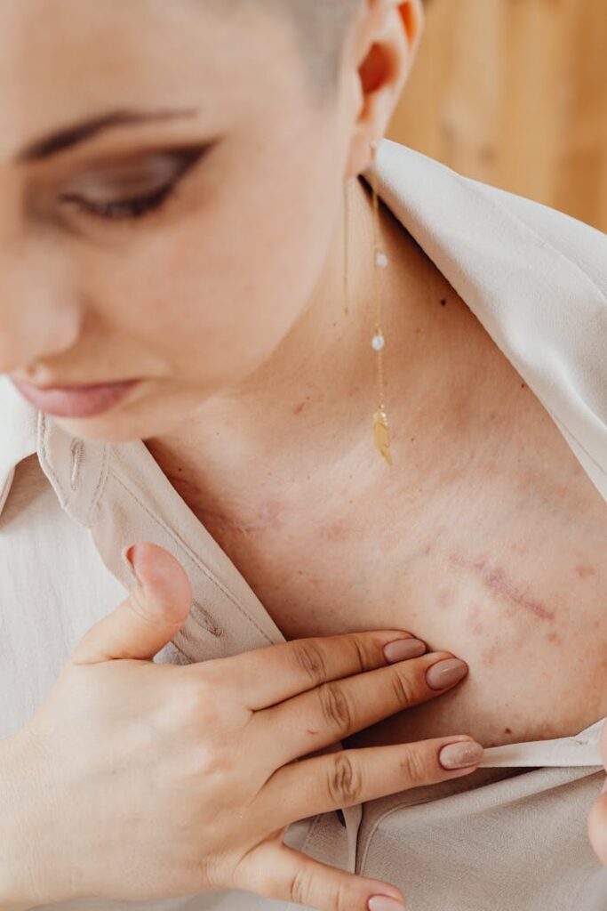 Close-up view of a woman gently touching a healing scar on her chest, showcasing strength and resilience.
